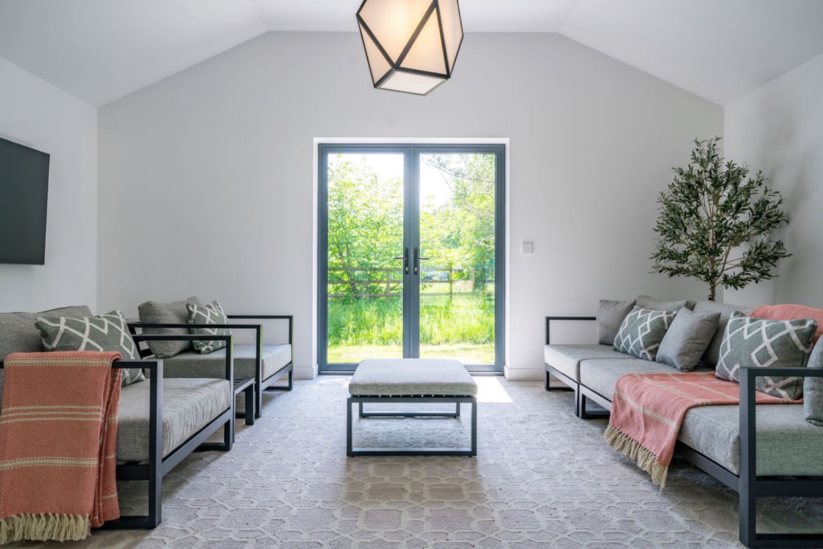 A light-filled garden room with symmetrical daybeds, woven throws and an olive tree framing the doors to the garden — an easy, restful space that draws the outside in.